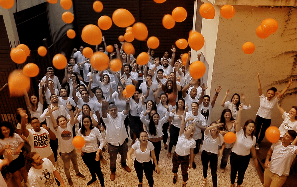 Foto com toda a equipe de branco lançando balões laranja para o céu